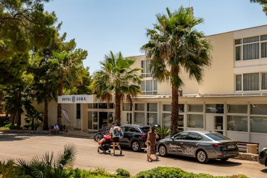 Hotel Zora in Primošten, Croatia, featuring palm trees and parked cars, under a bright summer sky.