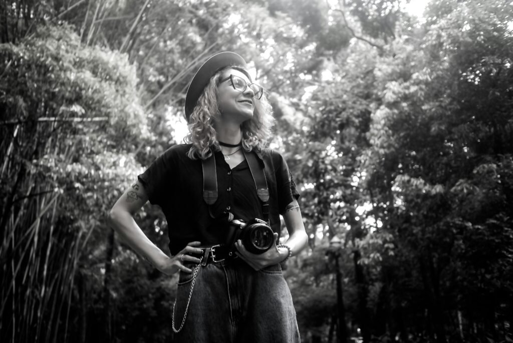 Black and white portrait of a confident photographer with her camera in a lush outdoor setting.